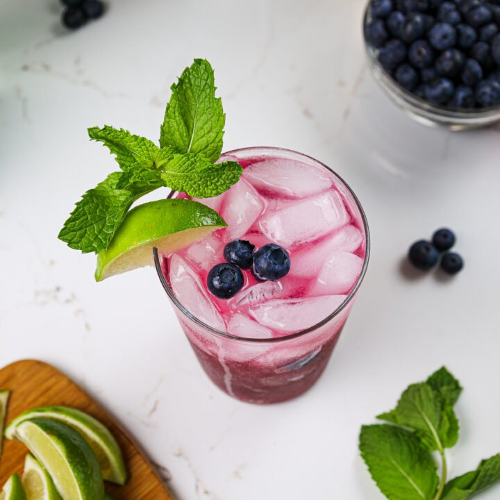蓝莓莫吉托的图像，上面饰有新鲜蓝莓，小树枝和柠檬楔的图像