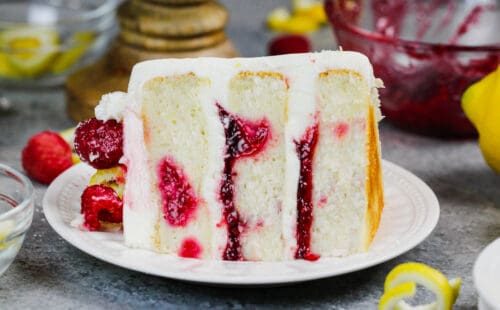 image of a slice of lemon rapsberry cake on a plate, showing it's raspberry filling and lemon cream cheese frosting