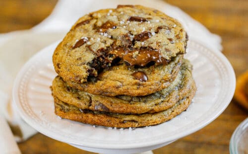 图片中是一堆棕色黄油巧克力曲奇饼，上面的曲奇被咬了一口，露出温暖融化的Nutella巧克力曲奇饼