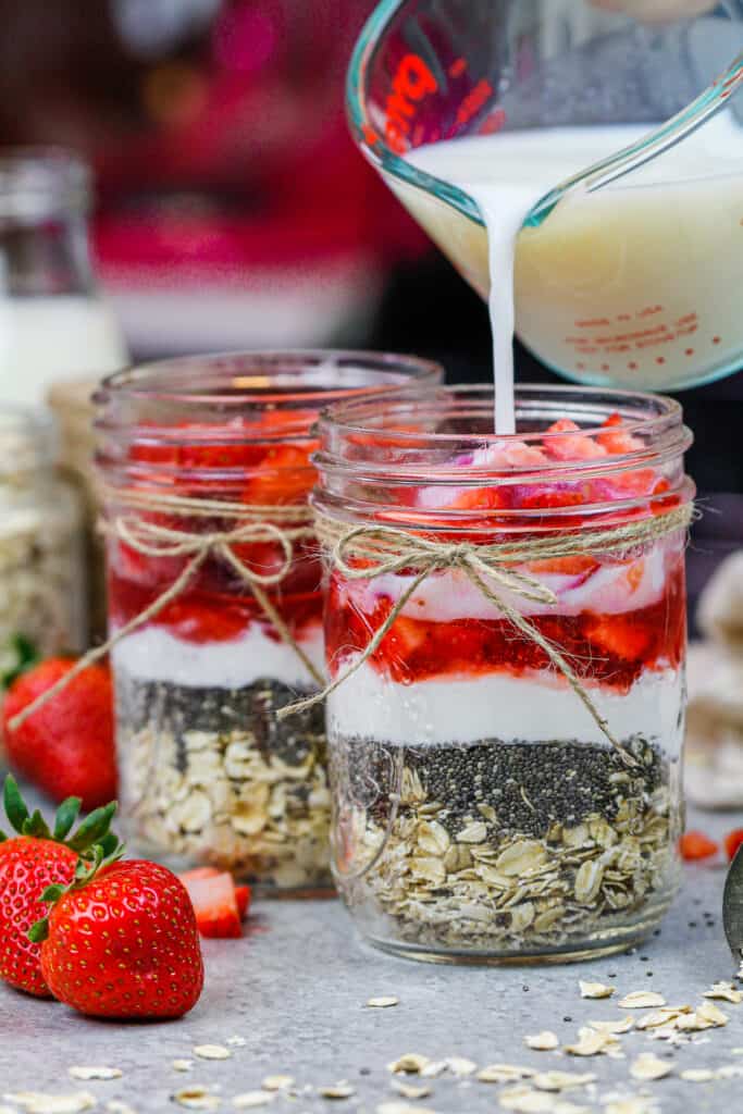 牛奶被倒进玻璃瓶，里面装满了制作草莓隔夜燕麦的原料