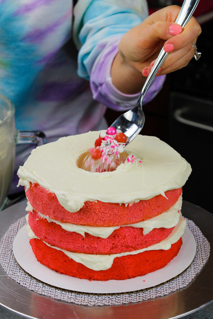 一个蓝色的渐变蛋糕被粉红色的糖果和糖屑填满，这是一个女孩的性别揭示蛋糕