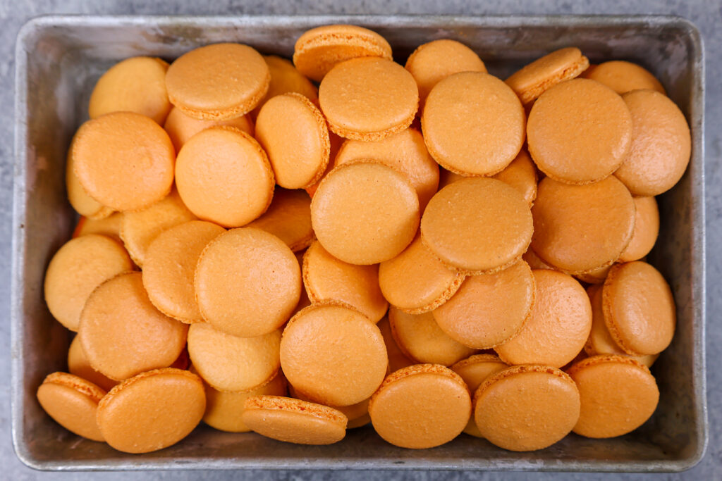 被烘烤和冷却的橙色macaron壳的盘子的图象被填装了