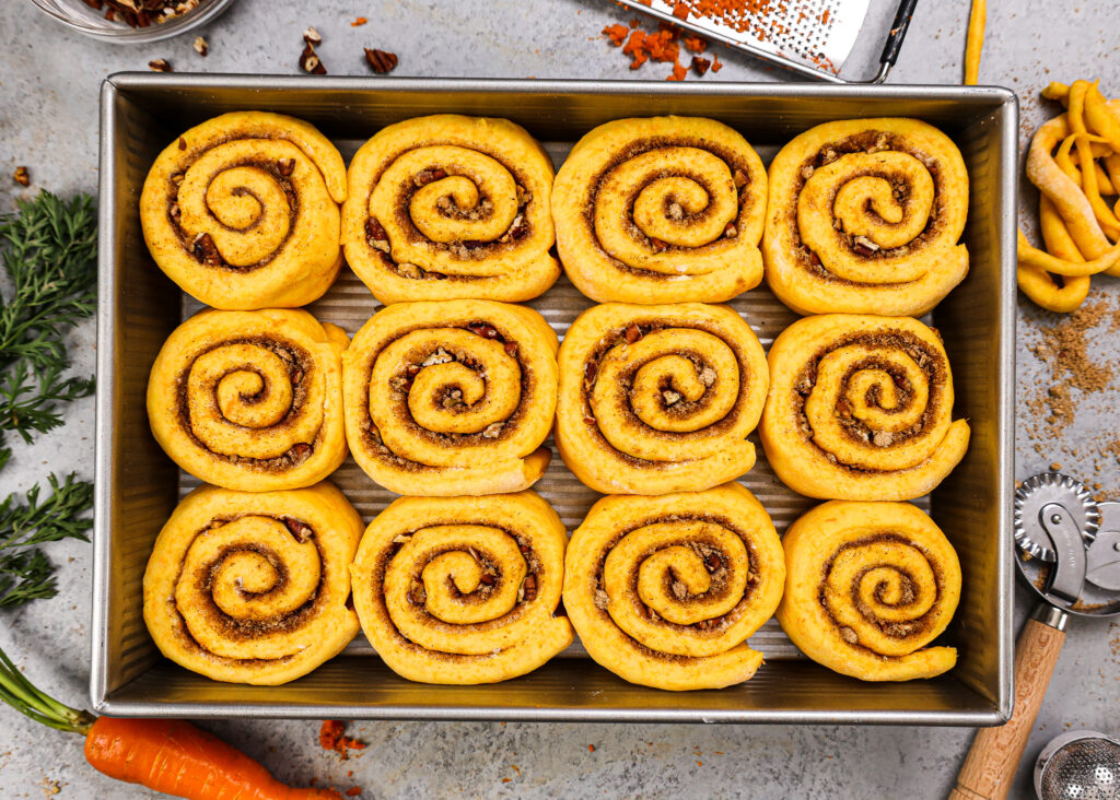 胡萝卜蛋糕肉桂卷的头顶镜头的图像，这些卷卷已经在9 x 13英寸的锅中证明并准备烘烤